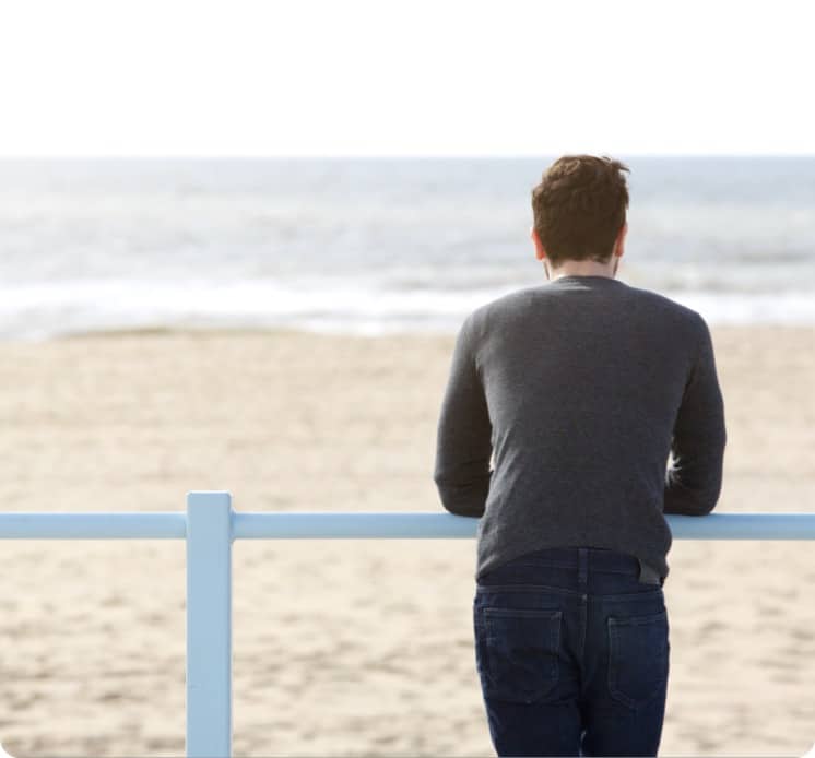 Young man standing alone looking at an empty beach